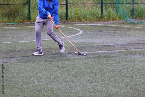 Obraz na płótnie An employee rakes water from the grass surface of a football field after rain. w salonie