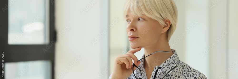 Woman with short hair looks out window holding glasses