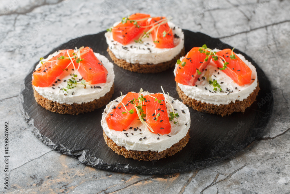 Healthy cheesecake sandwiches with red fish, cream cheese, sesame and microgreens close-up on slate plate on table. Horizontal