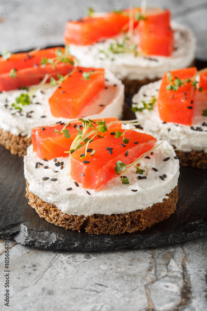 Canape sandwich with red fish, cream cheese, sesame and microgreens close-up on slate plate on table. Vertical Canape sandwich with red fish, cream cheese, sesame and microgreens close-up on slate plate on table. Vertical