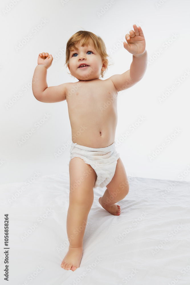Fist steps. Happy baby, little boy standing and raising hands as if celebrating small victory against white studio background. Concept of parenthood, natural beauty, love and care. Ad. Fist steps. Happy baby, little boy standing and raising hands as if celebrating small victory against white studio background. Concept of parenthood, natural beauty, love and care. Ad.