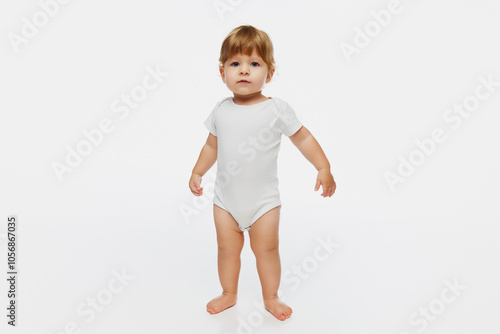 Curious baby standing with arms slightly raised, against white studio background, capturing innocence and wonder of early childhood. Concept of parenthood, natural beauty, love and care. Ad.