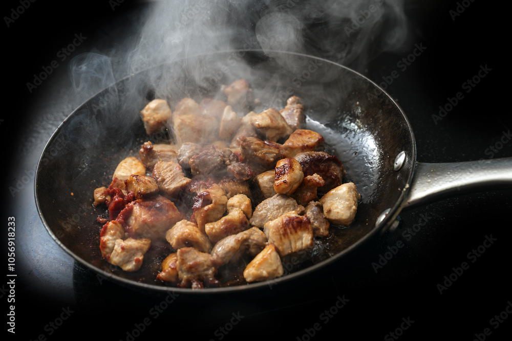 Diced pork is seared with tomato paste and a lot of steam in a cast iron frying pan, black background, copy space, selected focus in the middle Diced pork is seared with tomato paste and a lot of steam in a cast iron frying pan, black background, copy space, selected focus in the middle