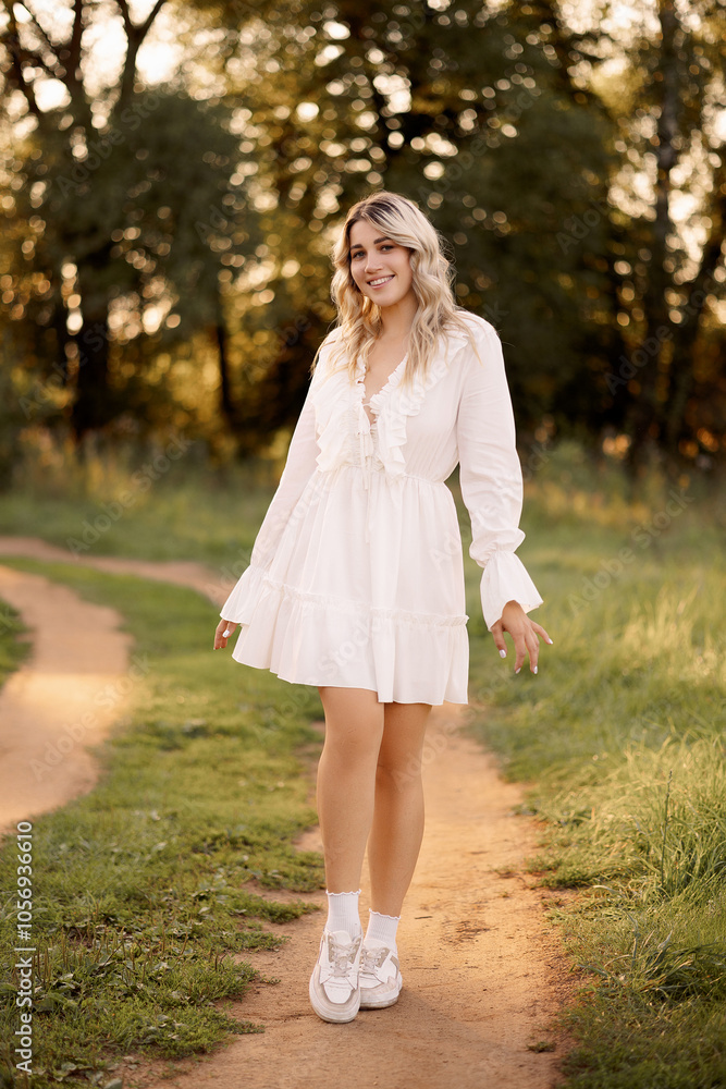 Beautiful young blonde woman in a white dress posing in the park. The concept of a summer fashion collection.