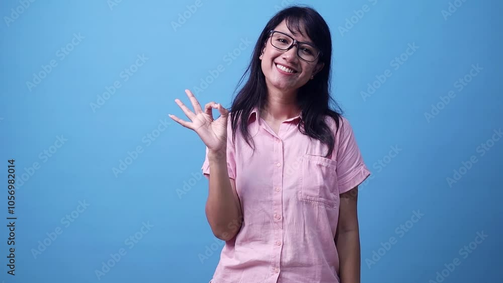 Young Asian woman is showing approval hand gesture for something. Isolated on blue background in studio. Young Asian woman is showing approval hand gesture for something. Isolated on blue background in studio.