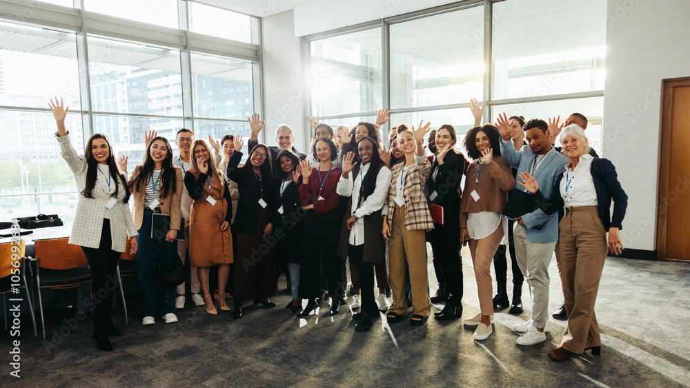 © Jacob Lund - Diverse group at seminar happily waving inside modern conference room with large windows and bright natural light