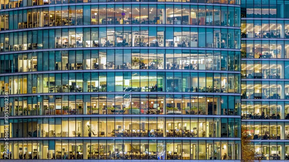 Timelapse panning view of an illuminated office building during evening with workers movement