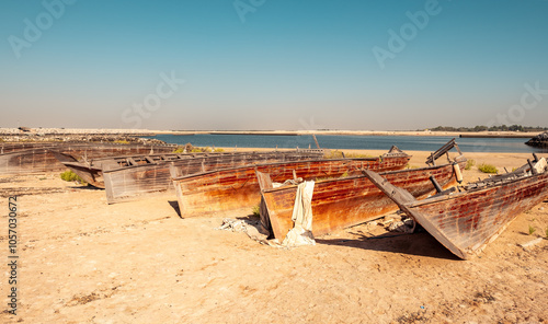 Old abandoned dhow boats standing in row on the shore of bay in UAE. Arabic traditional wooden boat. Old wooden boats left on land near the shore. Boats are badly worn and covered with rust photo