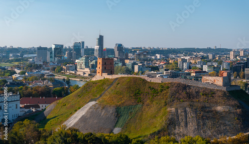 Aerial view of Gediminas' Tower on a hill in Vilnius, Lithuania, with the Neris River and modern high rise buildings in the background.