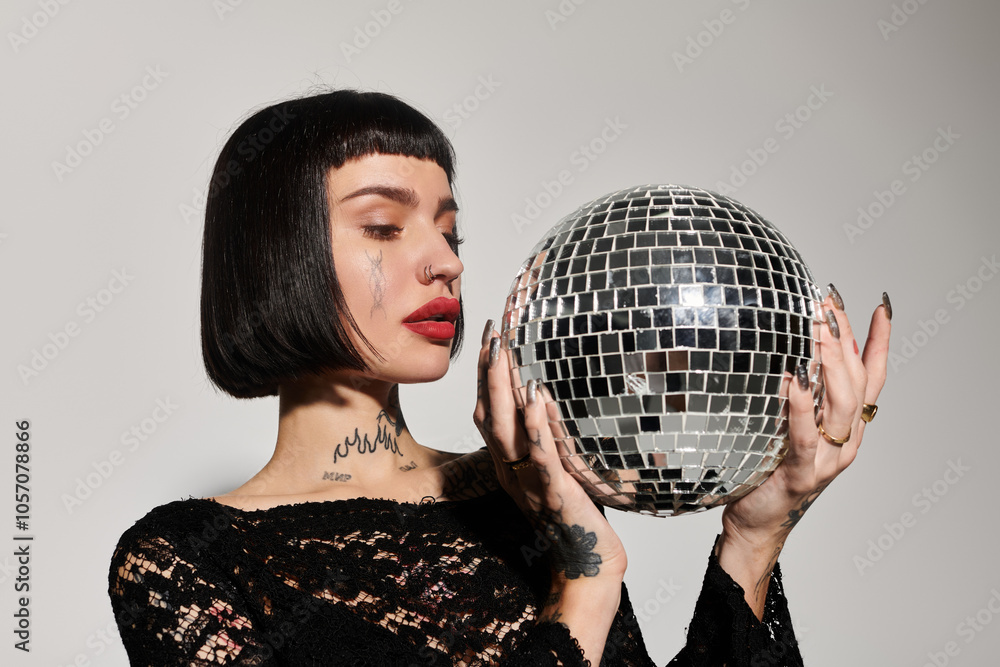 Naklejka premium Stylish woman with tattoos showcases a sparkling disco ball in a chic environment.
