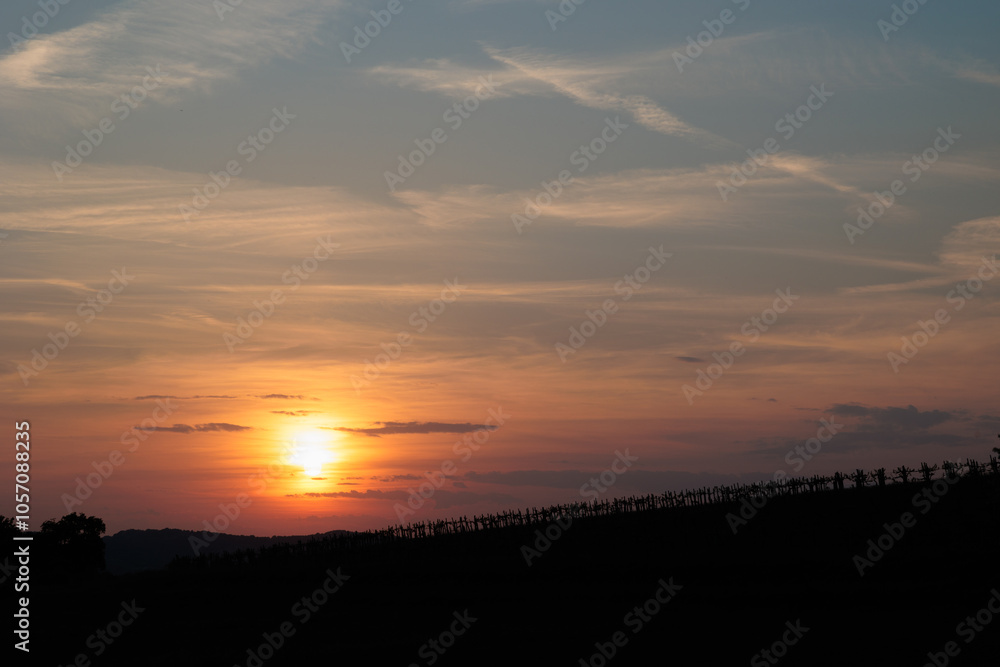 sole che tramonta dietro la sagoma di una collina e colora di arancione le nuvole leggere e la foschia nel cielo sole che tramonta dietro la sagoma di una collina e colora di arancione le nuvole leggere e la foschia nel cielo