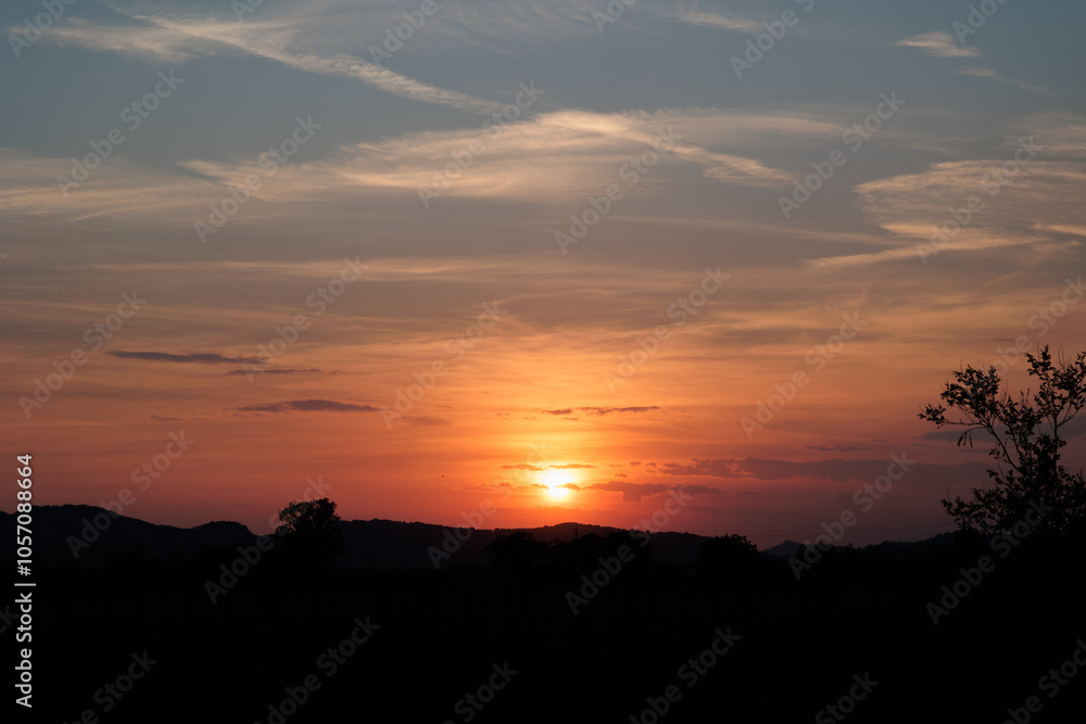 sole che tramonta dietro boschi e colline in un ambiente rurale e naturale di campagna e colora di arancione e rosso il cielo coperto da nuvole e da una foschia leggera sole che tramonta dietro boschi e colline in un ambiente rurale e naturale di campagna e colora di arancione e rosso il cielo coperto da nuvole e da una foschia leggera