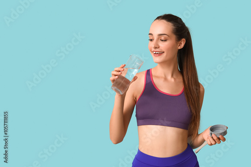 Beautiful young sporty happy woman with bottle of water on blue background