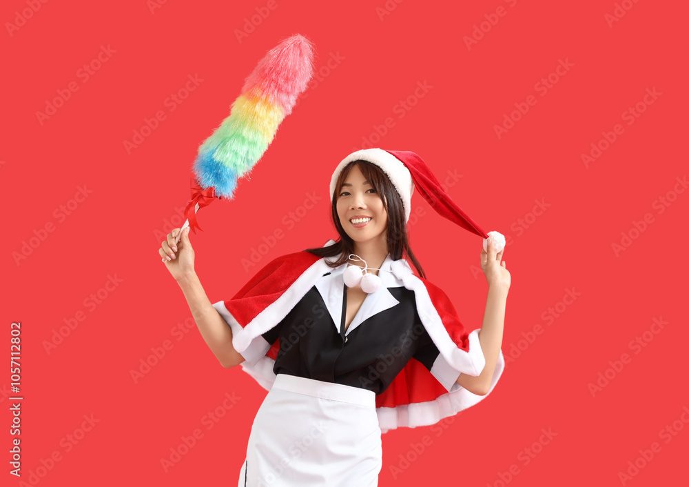 Female Asian chambermaid in Santa hat with pp-duster on red background Female Asian chambermaid in Santa hat with pp-duster on red background