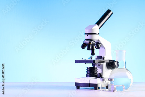 Modern microscope, ampules and laboratory flask with liquid on white table