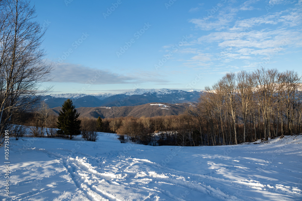 ampia vista panoramica di un ambiente che si estende tra le colline e le montagne innevate slovene, in inverno, durante un tramonto con cielo sereno, velato da qualche nuvola leggera ampia vista panoramica di un ambiente che si estende tra le colline e le montagne innevate slovene, in inverno, durante un tramonto con cielo sereno, velato da qualche nuvola leggera