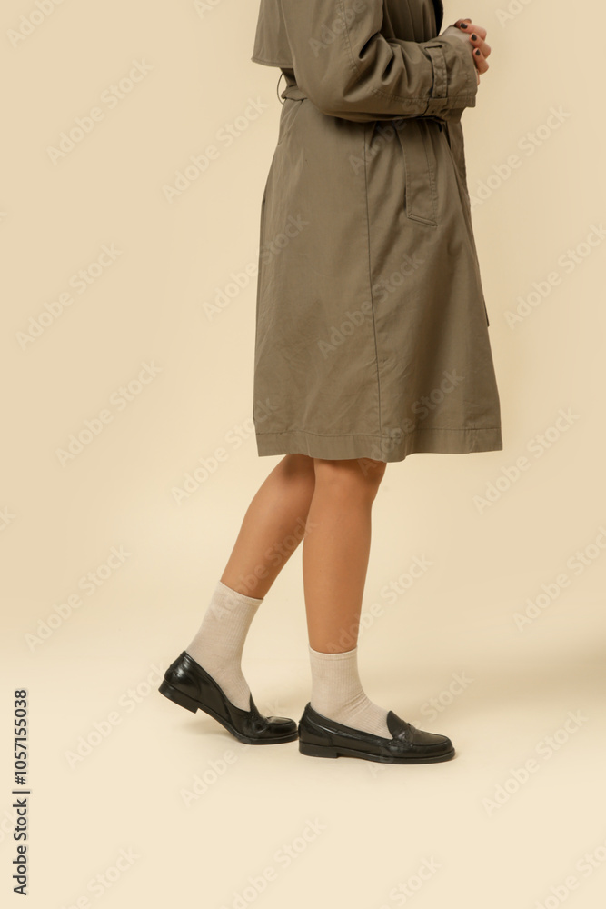 Woman wearing classic green trench coat and black leather moccasins with white socks, autumn fashion items. Woman wearing classic green trench coat and black leather moccasins with white socks, autumn fashion items.