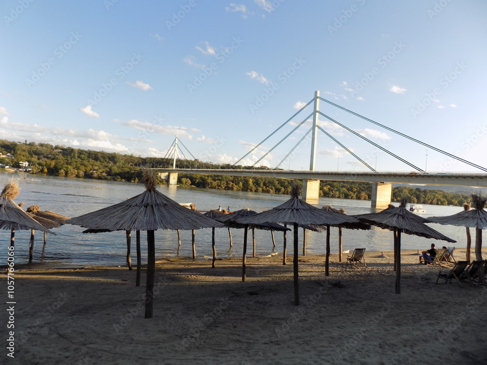 Fototapeta premium Parasols by the river with a bridge in the background.