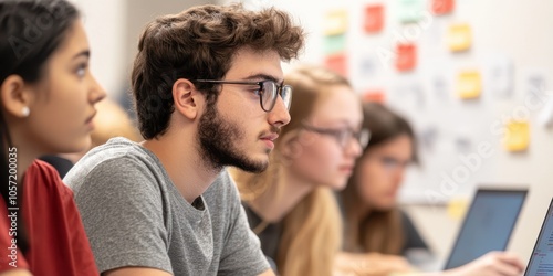 A focused group of students attending a class, engaged in learning, with laptops and notes in a modern classroom setting. photo