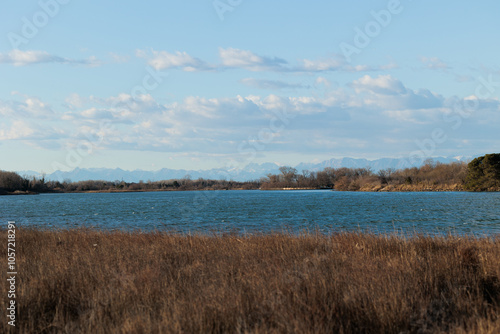 guardando da una delle sponde di un ramo del fiume Isonzo verso la pianura e le montagne distanti della regione Friuli Venezia Giulia, di giorno, con cielo parzialmente sereno, in inverno photo