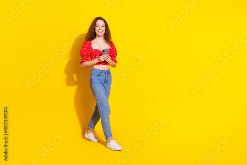 Full body photo of attractive young woman hold device walking dressed stylish red clothes isolated on yellow color background