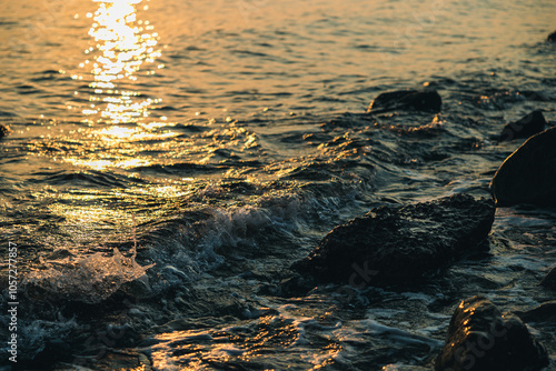 vista dettagliata delle piccole onde di marea di un mare tranquillo che bagnano la costa e le rocce al tramonto photo