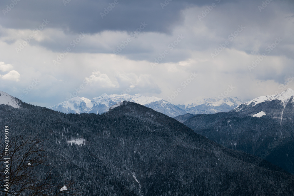 vista dettagliata di varie catene montuose lontane, completamente innevate, in un ambiente freddo e naturale di montagna nelle Alpi Italiane a nord est, sotto un cielo nuvoloso, in inverno