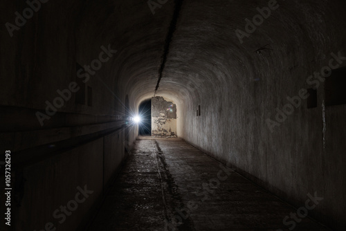 vista panoramica frontale ed in prospettiva di un'ampia, alta e lunga stanza vuota, dentro ad un vecchio bunker abbandonato, illuminata da una sola piccola luce photo