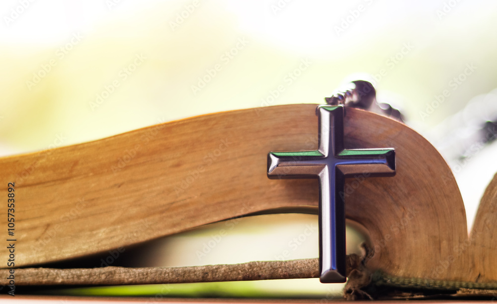 Obraz premium Dark metal cross on an old open book symbolizing the spread of Jesus Christs love among Christians reflecting faith devotion and the importance of Christian teachings.