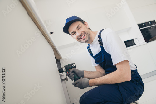 Smiling handyman in blue overalls using a cordless drill for home renovation in a modern kitchen setting