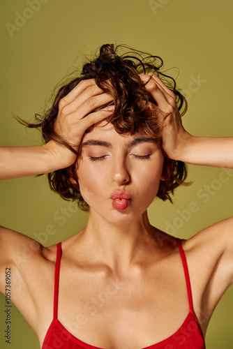 Obraz na plátně A young woman holds her head, showing a mix of emotions while playfully pouting her lips