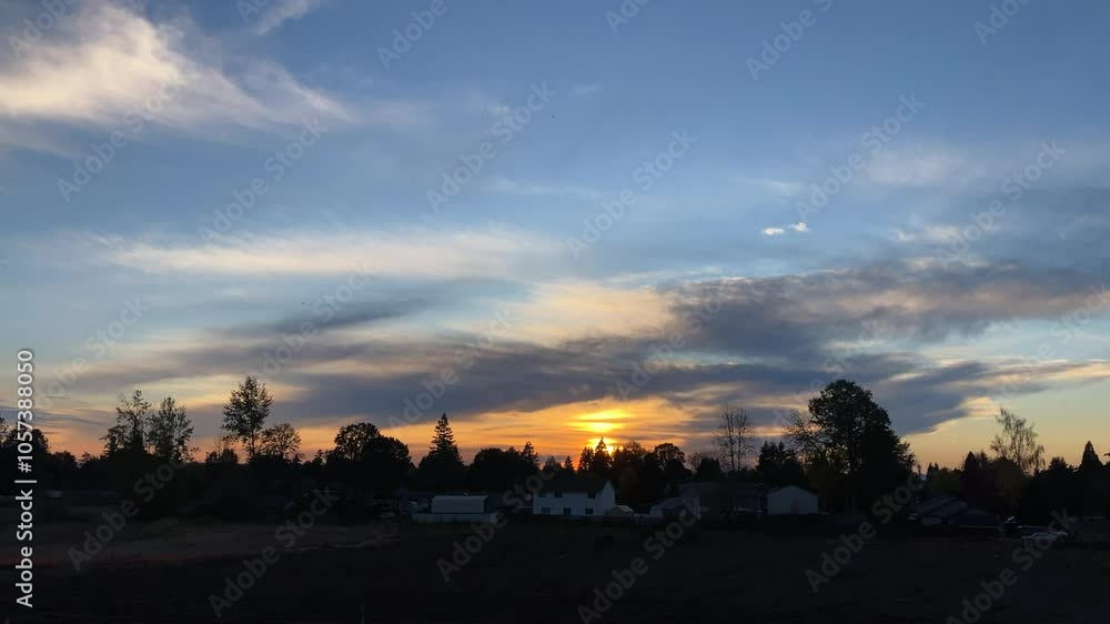 Sun falls behind tree cover hillside with smoke and fog dancing below colorful clouds in sky at dusk. Sun falls behind tree cover hillside with smoke and fog dancing below colorful clouds in sky at dusk.