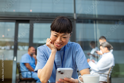 Medical female Asian professional using smartphone outside hospital during break photo