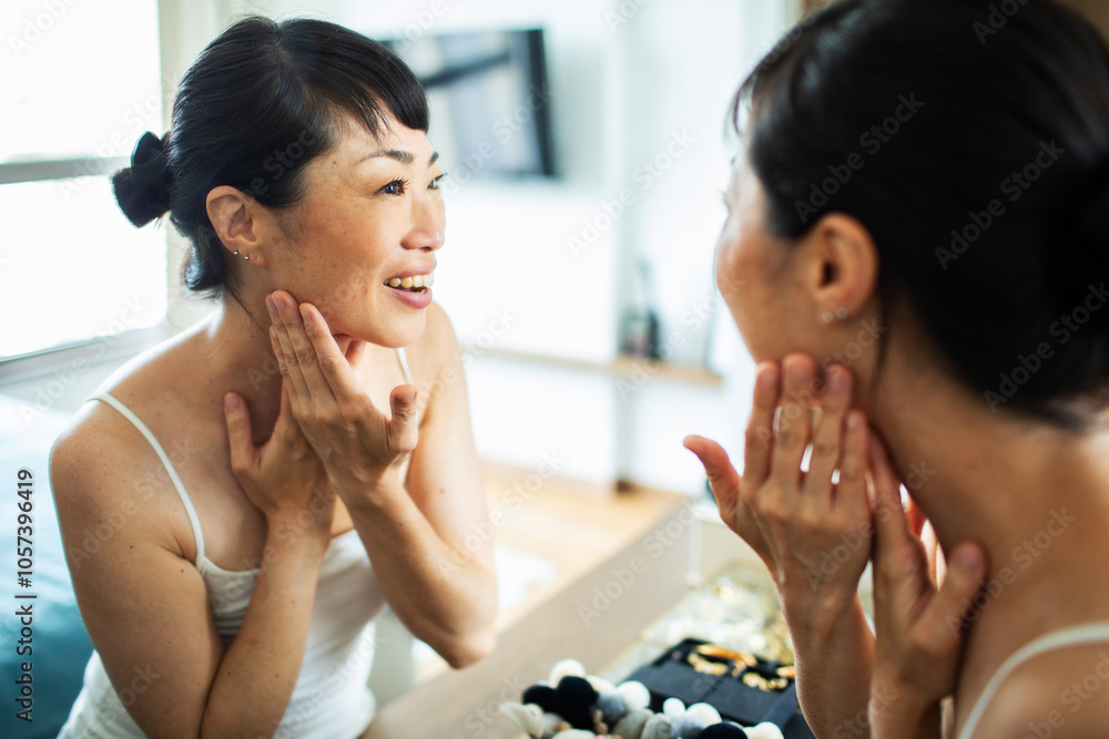 Asian woman examining her skin in the mirror at home Asian woman examining her skin in the mirror at home