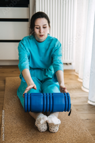 Young woman in blue clothing using foam roller for myofascial release and muscle tension relief. Physical therapy, relaxation, and self-care concept