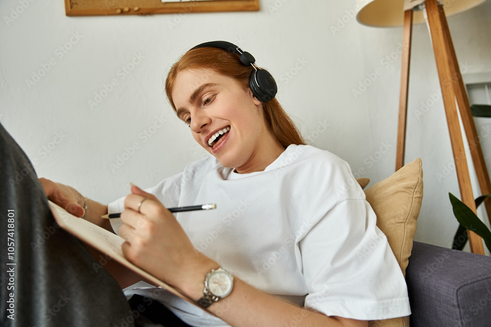 A young man smiles brightly while sketching in a notebook, immersed in his artistic process. A young man smiles brightly while sketching in a notebook, immersed in his artistic process.