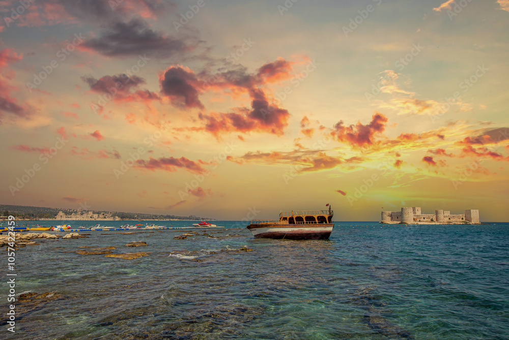 Maiden's Castle (Kız Kalesi) at sunset, with a boat stranded on the rocks on the beach in the foreground - Mersin, Turkey.