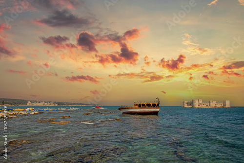 Obraz na płótnie Maiden's Castle (Kız Kalesi) at sunset, with a boat stranded on the rocks on the beach in the foreground - Mersin, Turkey. w salonie