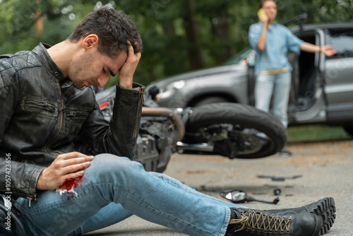 Motorcyclist sits on the asphalt near motorcycle, after road accidents with car. Broken and wrecked motorcycle on road