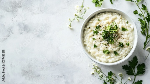 A white dish of creamy risotto topped with fresh herbs and parmesan cheese, top view. The risotto is rich and creamy, surrounded