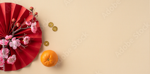 Festive Chinese new year flat lay with red folding fan, peach blossoms, gold coins, and an orange on a striped pastel backdrop photo