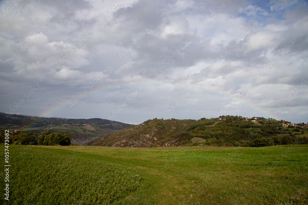 Obraz premium Idyllic valley view with rolling hills and a colorful rainbow, creating a serene landscape scene in the countryside.