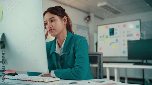 Asian businesswoman sitting at her desk is having a headache while working on her computer. She is feeling stressed and tired