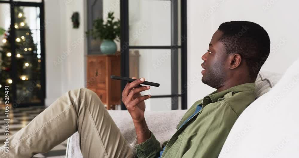 Relaxing at home, man using smartphone voice assistant near Christmas tree Relaxing at home, man using smartphone voice assistant near Christmas tree