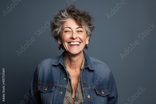 Portrait of a joyful woman in her 50s wearing a rugged jean vest over blank studio backdrop