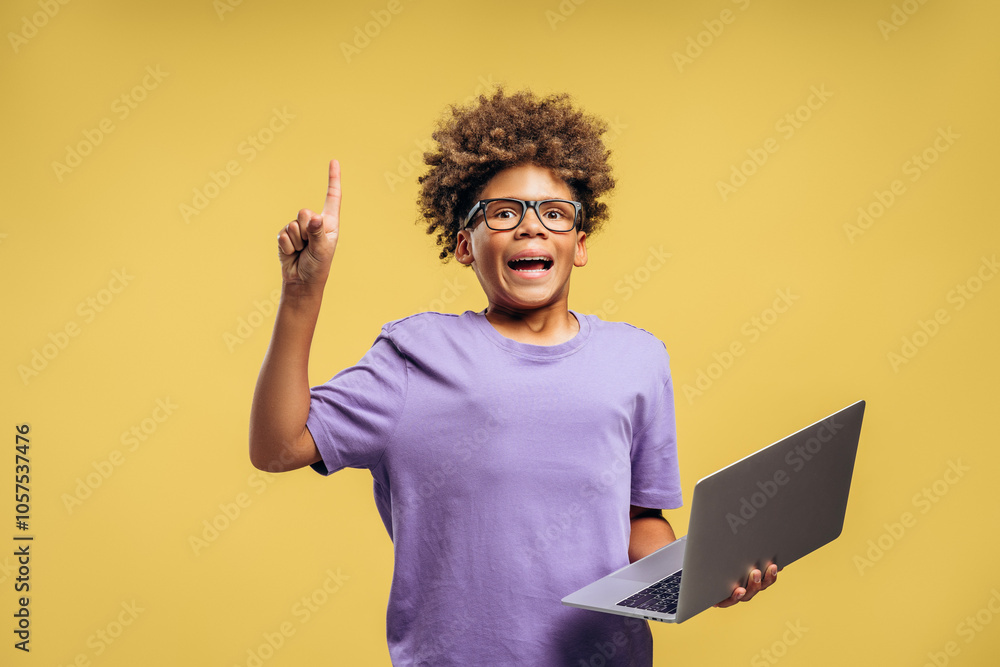 Happy African American boy, pupil wearing stylish eyeglasses, holding laptop pointing finger up Happy African American boy, pupil wearing stylish eyeglasses, holding laptop pointing finger up