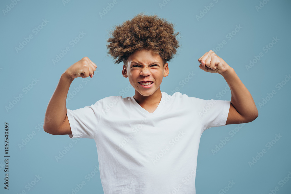 Strong, smiling African American boy with curly hair showing biceps on hands, looking at camera Strong, smiling African American boy with curly hair showing biceps on hands, looking at camera