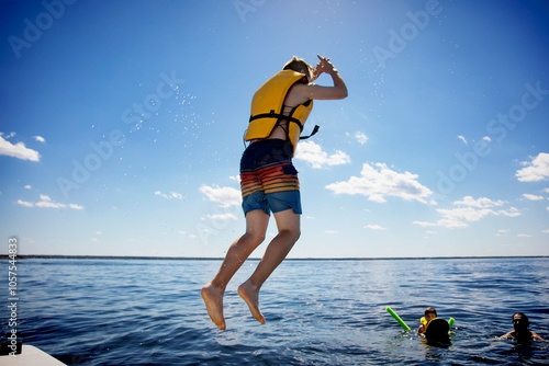 Young boy jumping off a boat and swimming in a lake with a lifejacket with his father and brother watching from the water, Lac Ste. Anne; Alberta Beach, Alberta, Canada photo