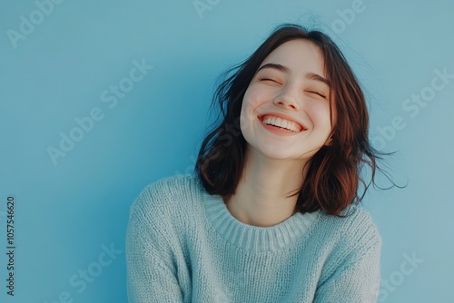 A cheerful woman wearing a pullover, smiling joyfully, her casual look complemented by the soft blue backdrop