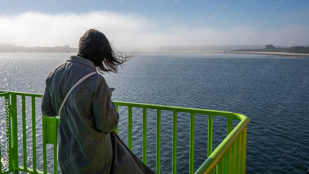 Female tourist using her smart phone as she rides a ferry into the fog across the Sado River from Setubal to Costa de Gale in Portugal; Portugal Female tourist using her smart phone as she rides a ferry into the fog across the Sado River from Setubal to Costa de Gale in Portugal; Portugal